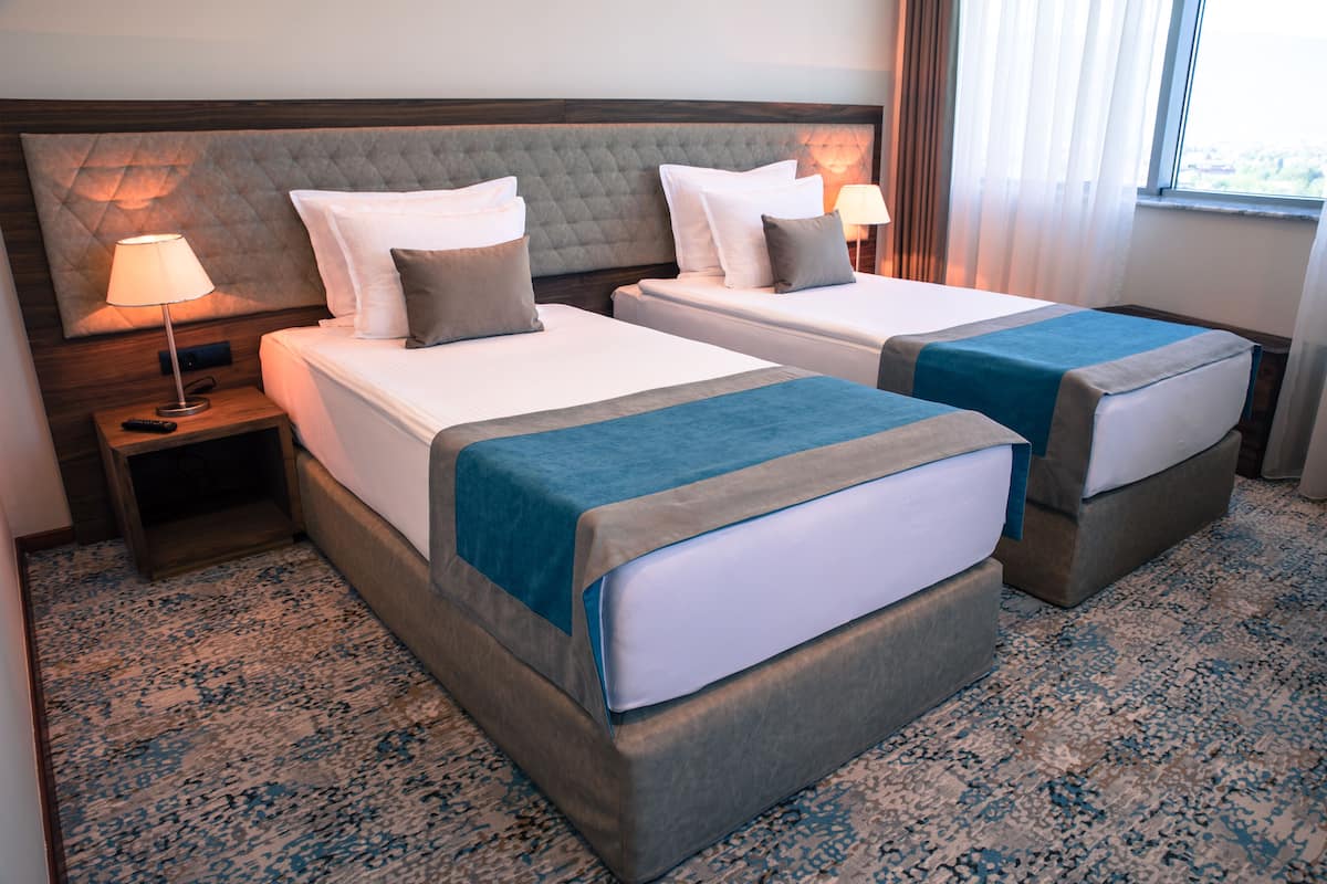 Una habitación de hotel con dos camas, un cabecero grande, una mesita de noche con lámpara y una alfombra estampada.