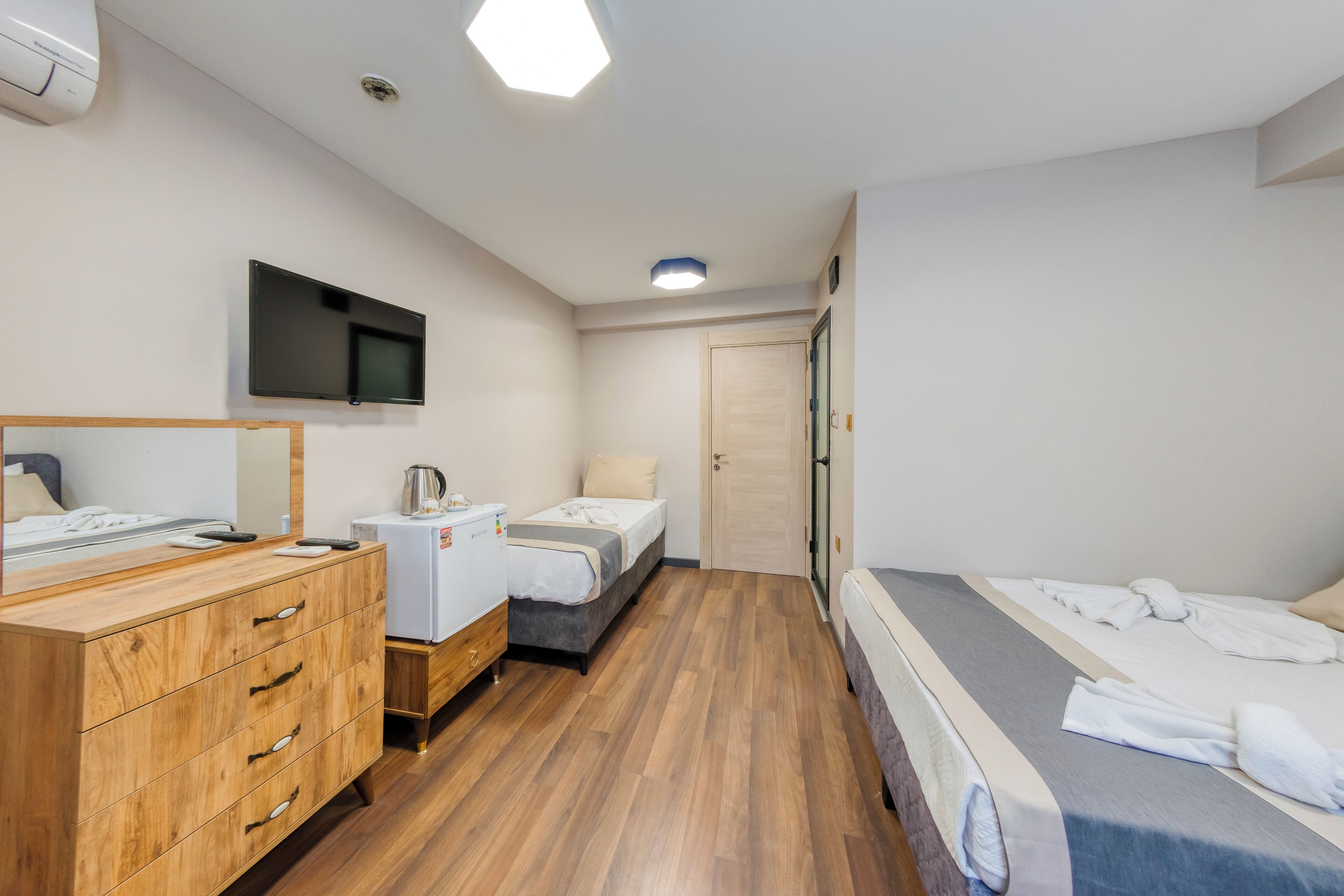 A hotel room with a wooden dresser, a bed, a television, and a door.