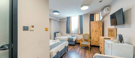 A hotel room with two beds, a wooden wardrobe, a desk with a kettle, a chair, and a TV mounted on the wall.