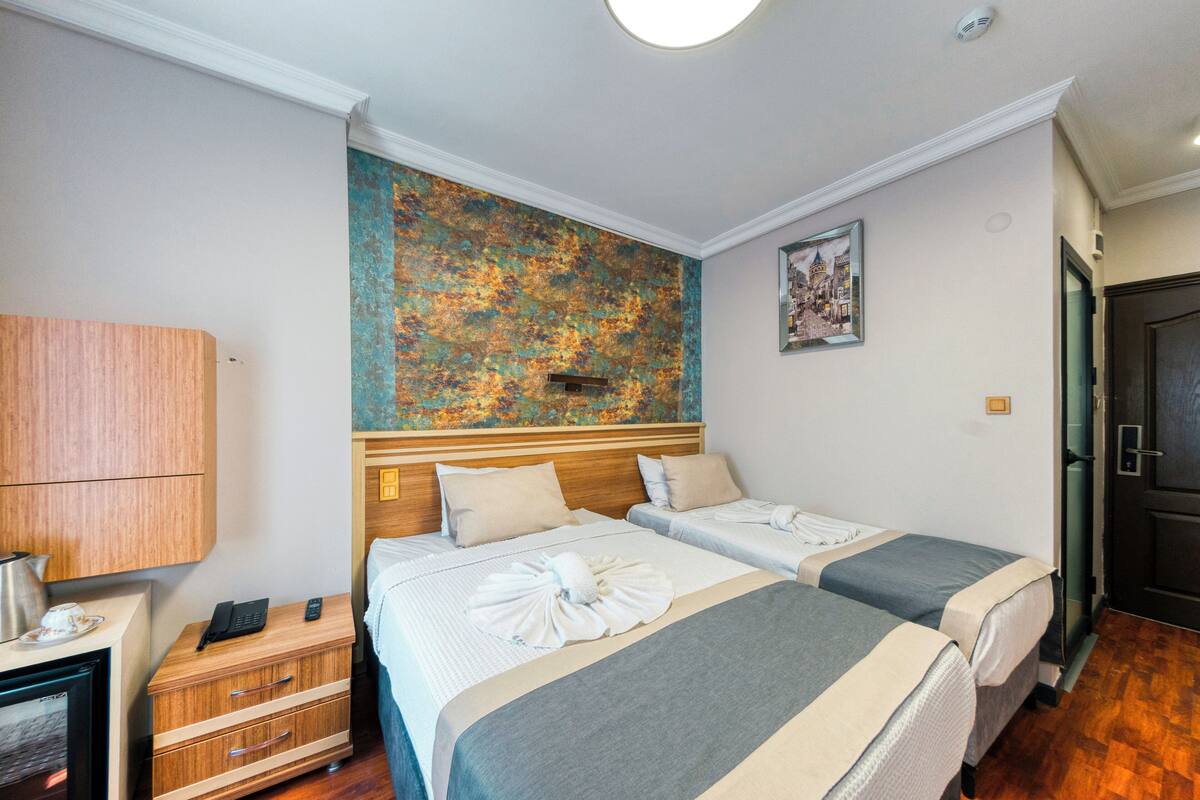A hotel room with two beds, a wooden nightstand, a small table with a kettle, and a decorative wall.