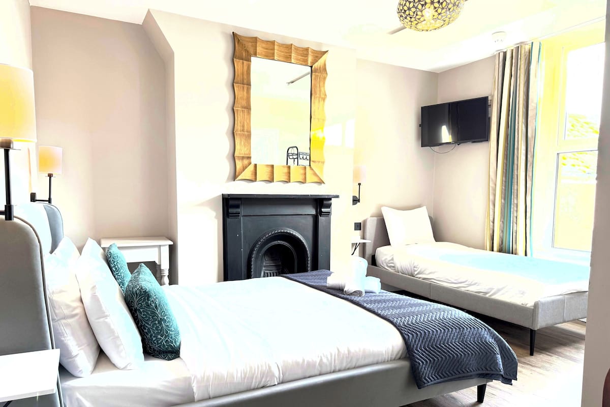A hotel room with a large bed, a smaller bed, a fireplace, a TV, and a window with curtains.