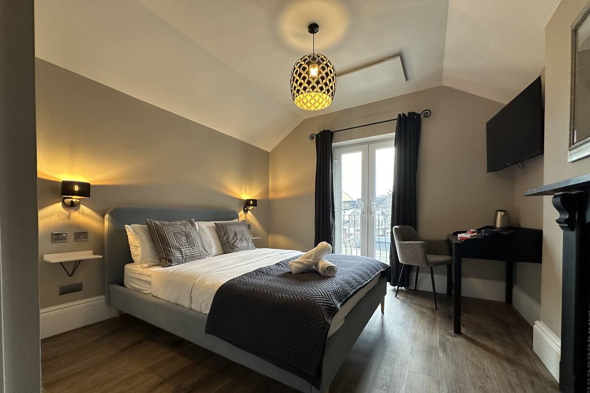 A bedroom with a bed, bedside lamps, a desk, a chair, and a television.