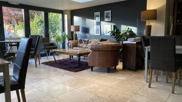 A modern living room with a sofa, coffee table, and chairs, a dining area with a table and chairs, and a large window with a view of trees.