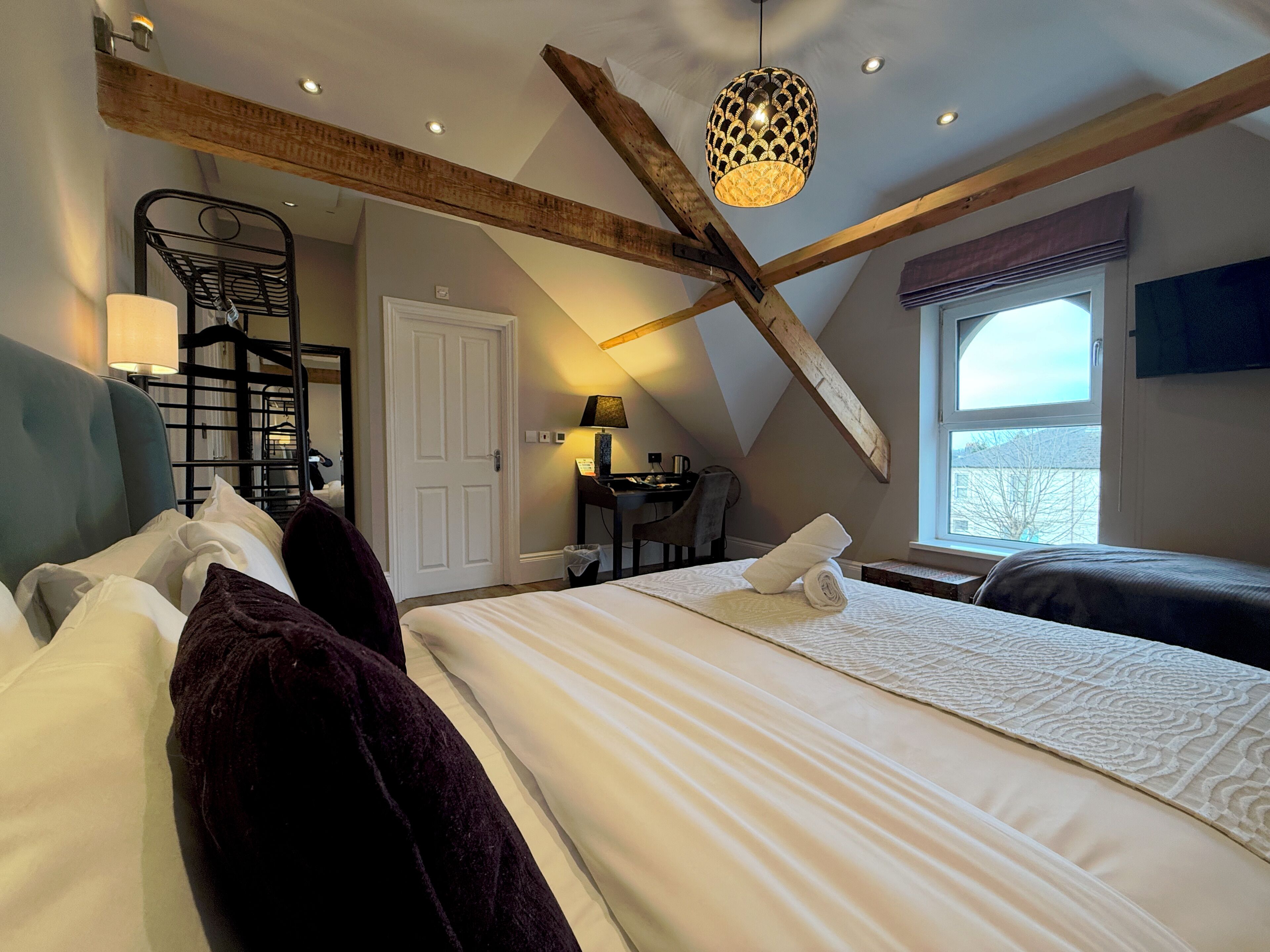 A bedroom with two beds, a desk, a chair, a window with a view, and a staircase.