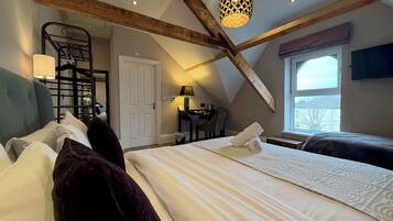 A bedroom with two beds, a desk, a chair, a window with a view, and a staircase.
