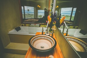 A bathroom with a large bathtub, a sink with a decorative bowl, and a mirror reflecting a scenic view.