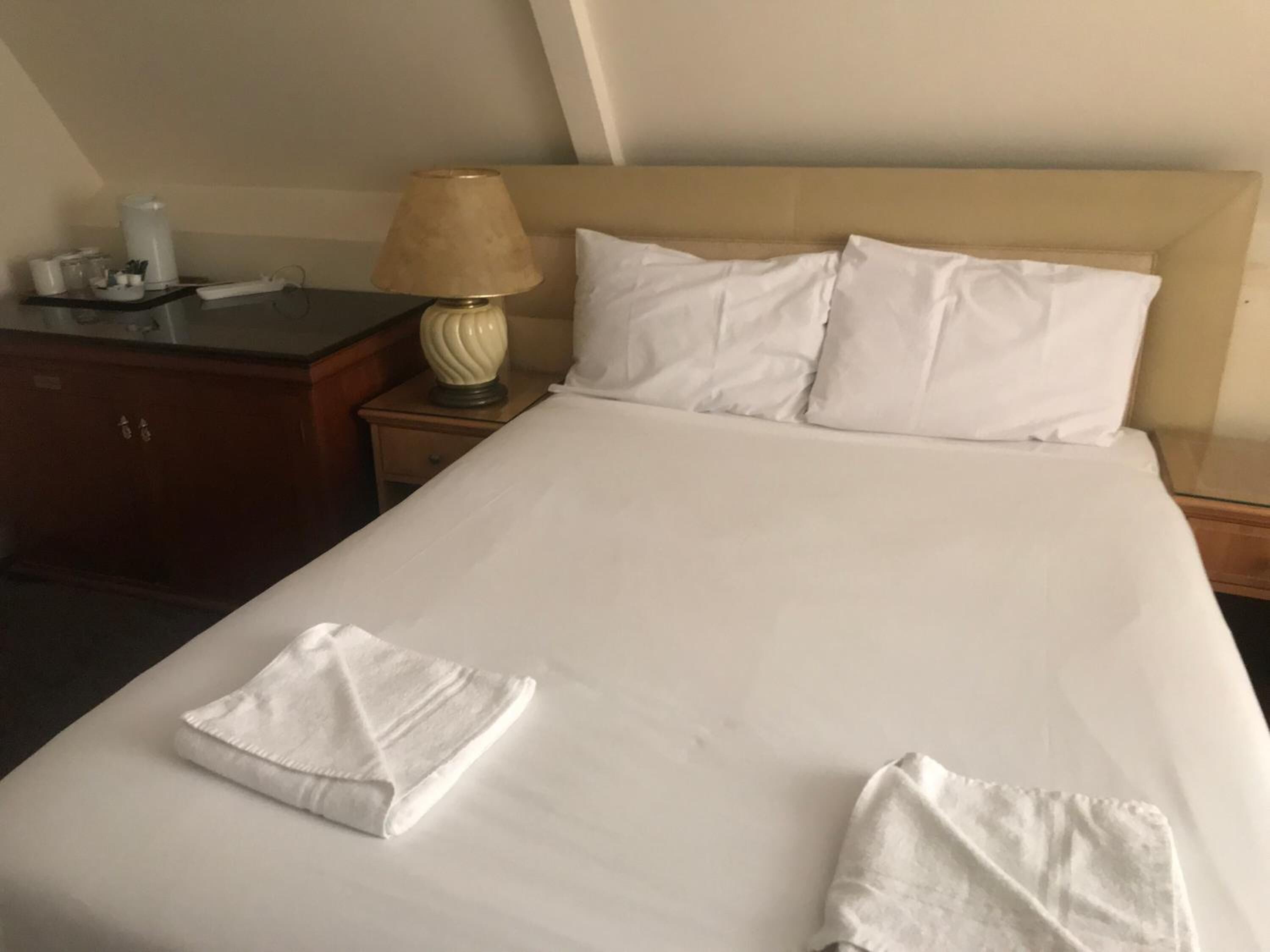 A neatly made bed with white linens, a bedside lamp, and a wooden nightstand.