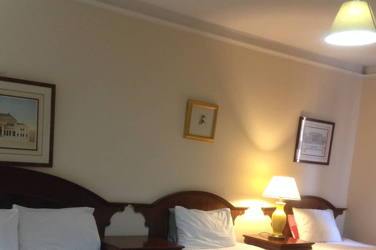 Ein Hotelzimmer mit zwei Betten, jeweils mit weißen Bettwäsche und Kissen, einem hölzernen Kopfteil und einem Nachttisch mit Lampe.