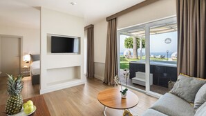 A modern hotel room with a flat-screen TV, a wooden table with fruits, a sofa, and a balcony with a view of the sea. - LABRANDA Rocca Nettuno Tropea (Tropea)