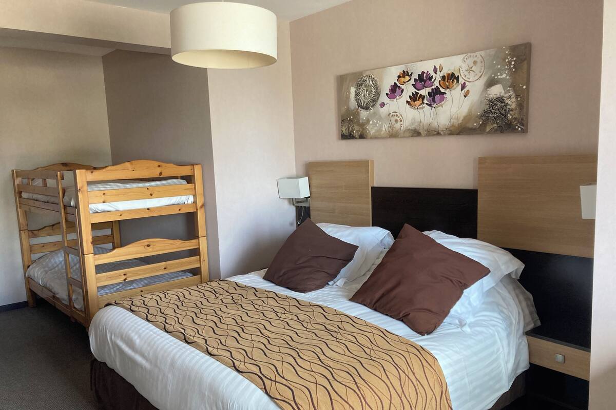 Une chambre d’hôtel avec un lit superposé, un lit simple avec des oreillers marron, une couverture à motifs, une horloge murale et un tableau décoratif.