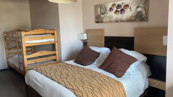 Een hotelkamer met een stapelbed, een enkel bed met bruine kussens, een geborduurd plaid, een wandklok en een decoratief schilderij.
