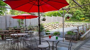 An outdoor patio with tables and chairs, red umbrellas, and a stone wall. - The Originals Relais, Auberge de la Petite Ferme (Besse-et-Saint-Anastaise)