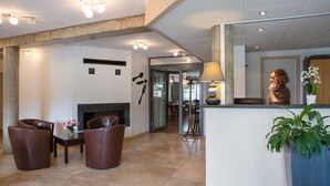 A modern lobby with a fireplace, leather chairs, a reception desk, and a large mirror. - The Originals Relais, Auberge de la Petite Ferme (Besse-et-Saint-Anastaise)
