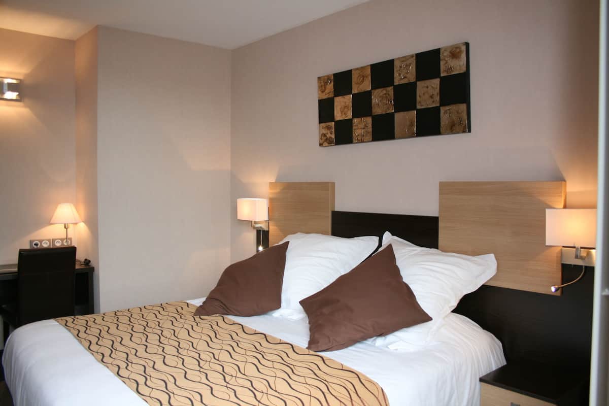 Une chambre d’hôtel avec un lit bien fait, deux lampes de chevet, une œuvre d’art accrochée au mur et une petite table avec une lampe.