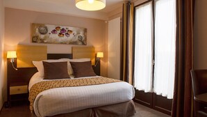 A hotel room with a large bed, two bedside lamps, a headboard with a floral artwork, and a view of the outside through large windows. - The Originals Relais, Auberge de la Petite Ferme (Besse-et-Saint-Anastaise)
