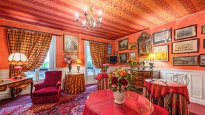 A room with a red carpet, a red armchair, a round table with a vase of flowers, and a chandelier. - Hotel De Nice (Paris)