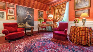 A room with a red armchair, a wooden desk, a patterned rug, and a large painting on the wall. - Hotel De Nice (Paris)