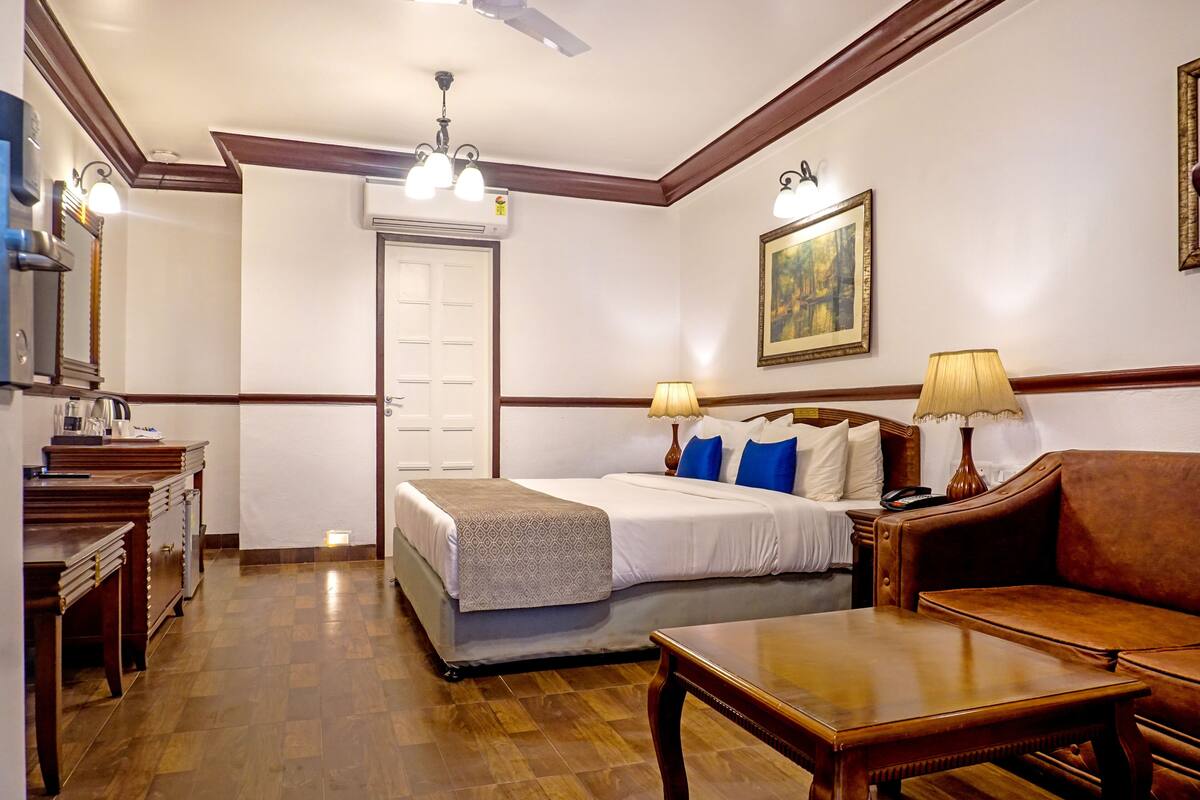 A hotel room with a bed, bedside table, lamp, and a wooden floor.
