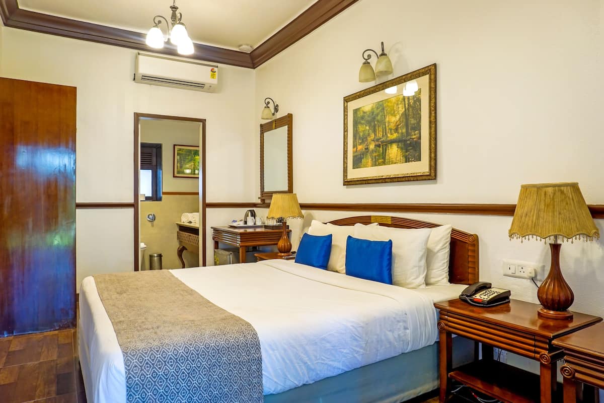 A hotel room with a large bed, bedside table with a lamp, a telephone, and a mirror on the wall.
