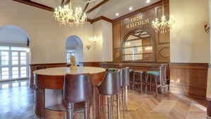 A bar area with a round table and multiple stools, a chandelier, and a sign reading "1828 MALCOLM". - Citrus Chambers Mahabaleshwar (Mahabaleshwar)