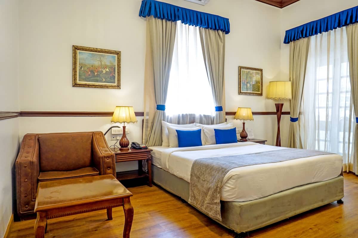 A hotel room with a large bed, a wooden chair, two bedside tables with lamps, and curtains.