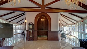A spacious lobby with a high ceiling, wooden beams, a grand chandelier, and a large arched doorway. - Citrus Chambers Mahabaleshwar (Mahabaleshwar)