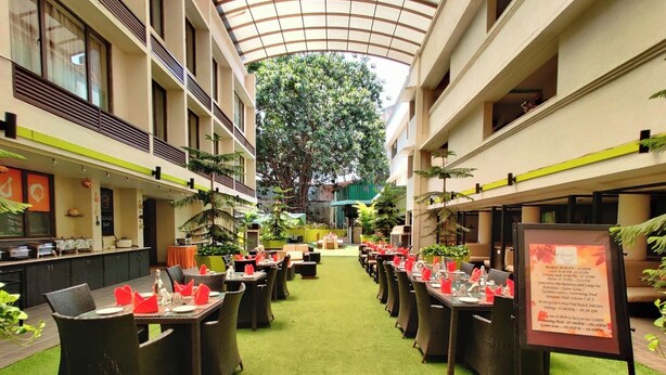 A hotel atrium with a central green carpet, dining tables with red napkins, and a menu board on the right. - Citrus Hotel Lonavala (Mawal)