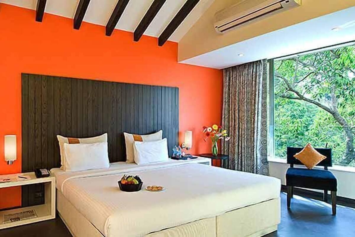 A hotel room with a large bed, a nightstand, a chair, and a window with a view of trees.