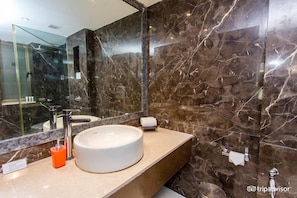 A modern bathroom with a large mirror, a round sink, and marble walls.