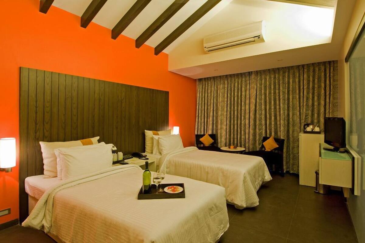 A hotel room with two beds, a desk, a TV, and a window with curtains.