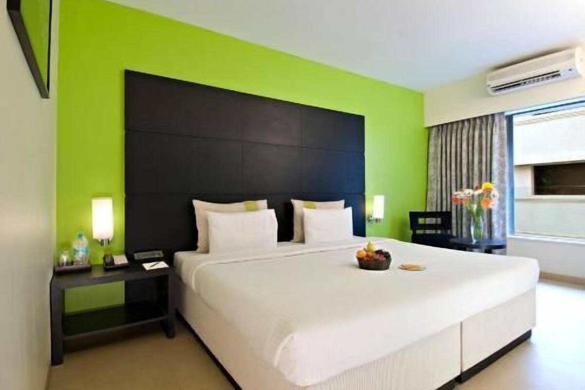 A hotel room with a large bed, a nightstand, a lamp, and a window with curtains.