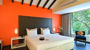 A hotel room with a large bed, a nightstand, a chair, and a window with a view of greenery. - Citrus Hotel Lonavala (Mawal)