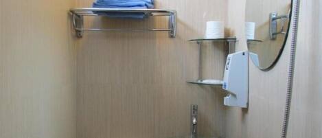A compact bathroom with a toilet, a glass sink, a handheld showerhead, and a mirror.