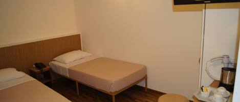 Une chambre d’hôtel avec deux lits simples, une tête de lit en bois, une table de chevet avec un téléphone, un bureau avec une machine à café et un téléviseur fixé au mur.