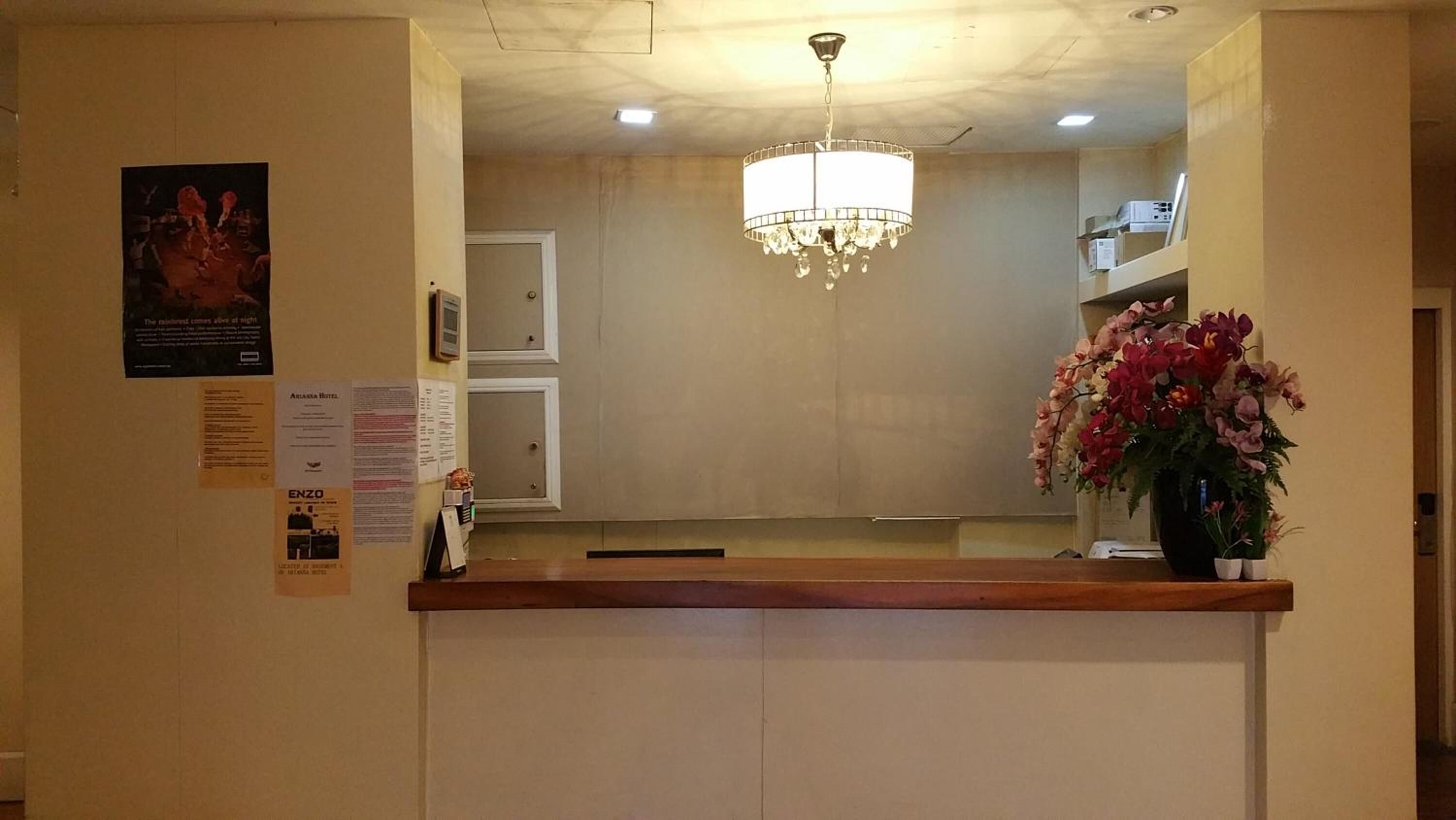 Zona de recepción de un hotel con una araña, un arreglo floral y carteles informativos en la pared.