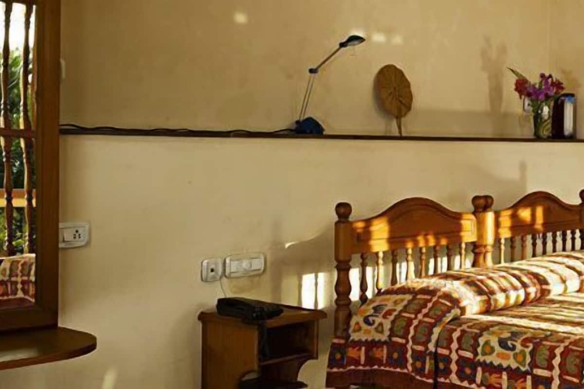 Un dormitorio con una cama de madera, una mesita de noche, una lámpara, una estantería con un jarrón de flores y un cuadro en la pared.