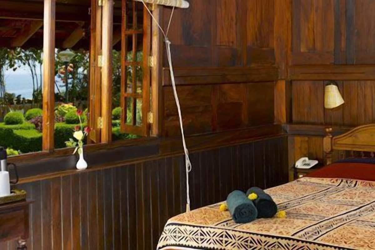 Una habitación de madera con una cama, una mesita de noche, una lámpara y vistas al verdor exterior.