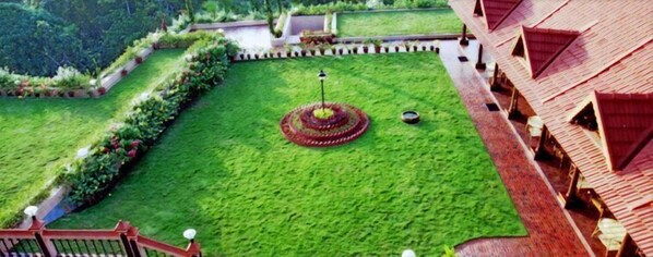 A well-maintained garden with a circular fountain, a pathway, and a building with a red roof. - Thapovan Heritage Home (Neyyattinkara)