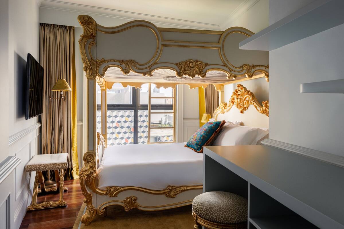 Un'elegante camera da letto con un letto a baldacchino, una piccola panca, una televisione e vista sulla città attraverso una finestra.