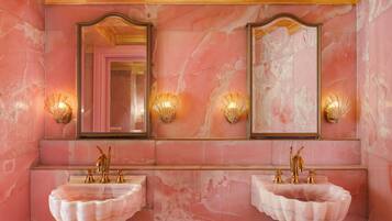 A bathroom with two marble sinks, gold fixtures, and wall-mounted mirrors with sconces.