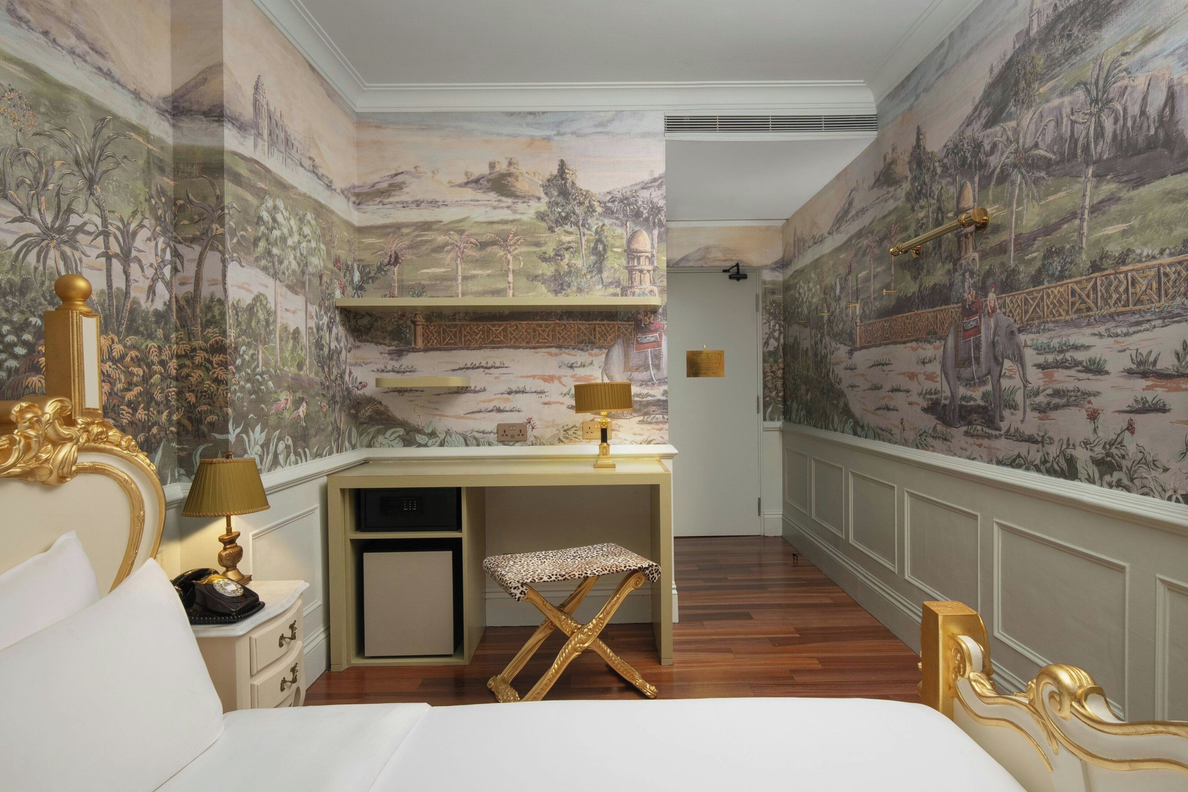 Un dormitorio con cama, escritorio y silla. La habitación tiene un mural en las paredes.