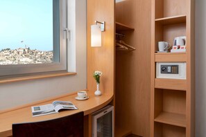 Habitación de hotel con un escritorio de madera, una cafetera, una taza de café, un florero con flores y vistas a un paisaje urbano.