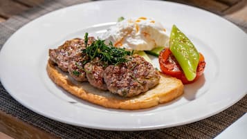 A plate of food with a meat patty, a slice of bread, and a grilled vegetable, accompanied by a bowl of salad.