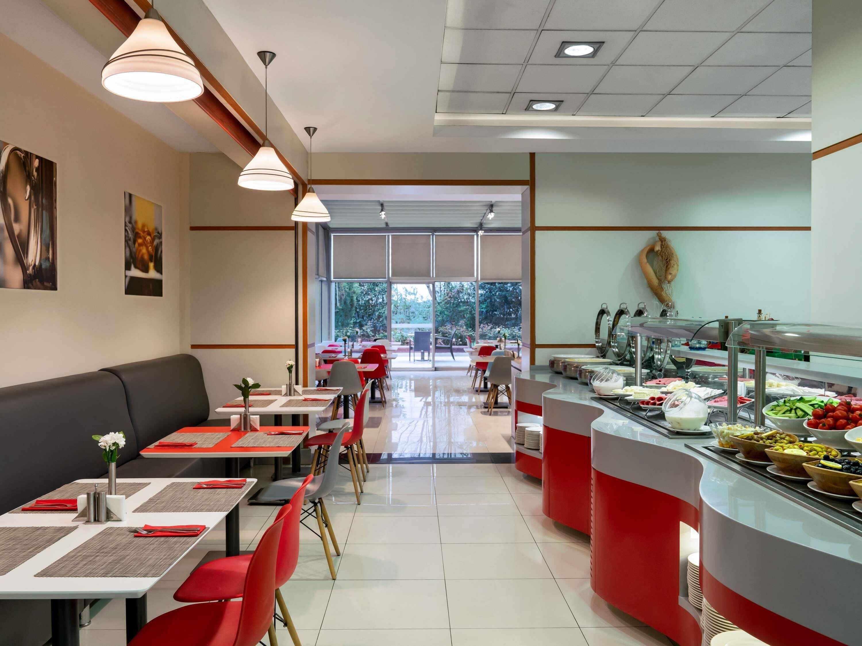 A modern restaurant with red and white decor, multiple dining tables, and a buffet area.