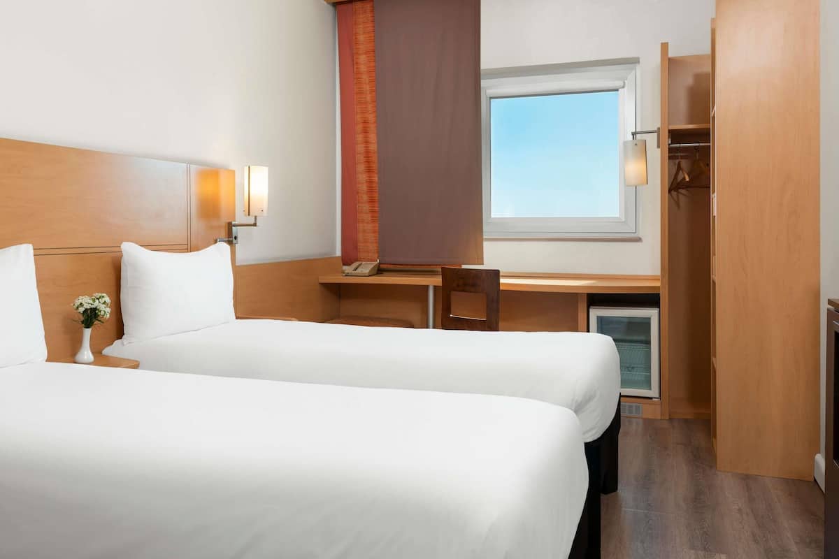 Habitación de hotel con dos camas, un escritorio, una silla, un teléfono y una ventana.