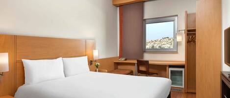 A hotel room with a large bed, a desk, a chair, a TV, and a wardrobe.