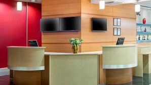 A reception area with two reception desks, a red wall, and a wooden panel design. - ibis Gaziantep (Gaziantep)