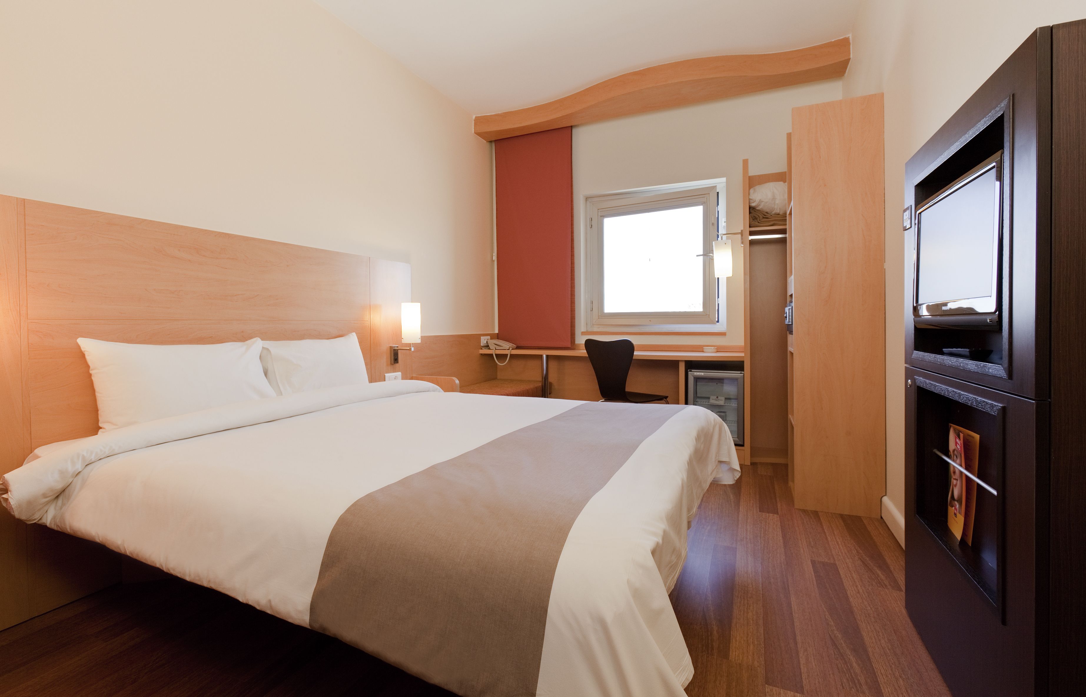 Una habitación de hotel con una cama grande, un escritorio, una silla, un armario y un televisor.