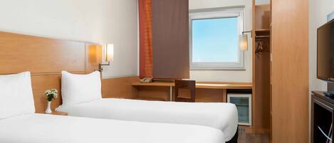 A hotel room with two beds, a desk, a TV, a wardrobe, and a window.
