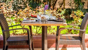 An outdoor dining table with food and drinks, surrounded by wicker chairs and greenery. - ibis Gaziantep (Gaziantep)